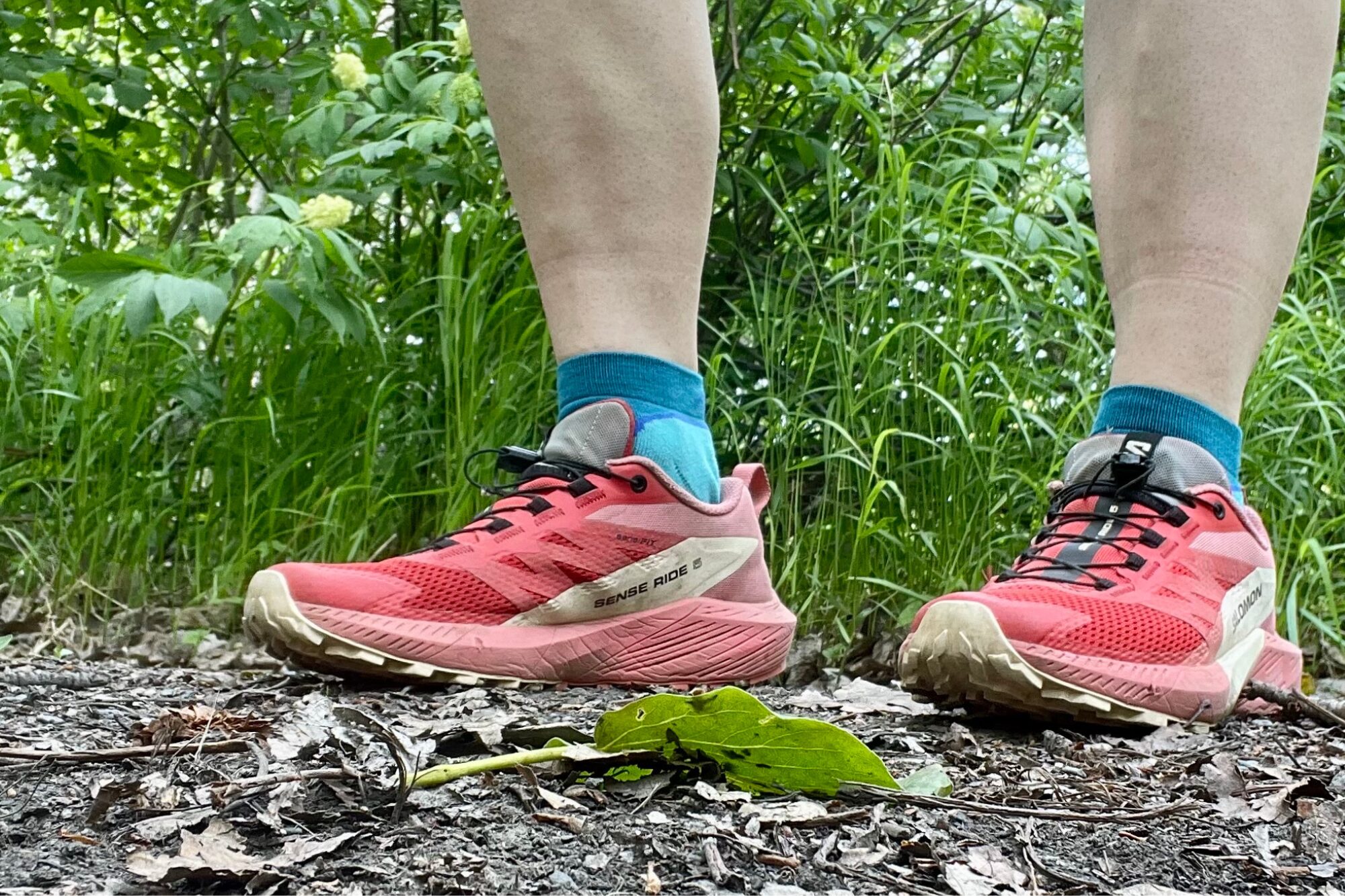 A hiker wears blue ankle socks with pink Salomon running shoes while out on the trail.