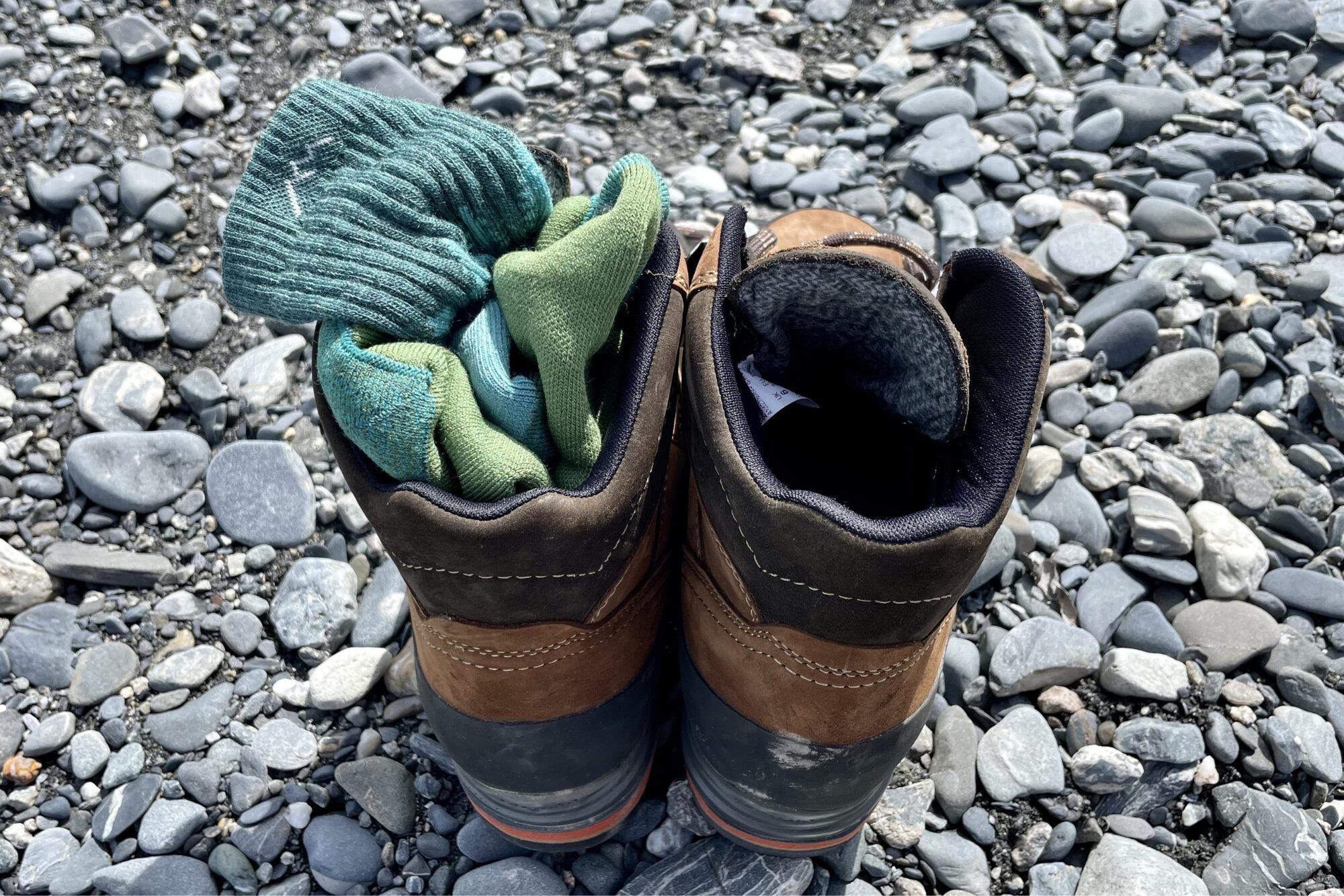 A pair of darn tough socks are stuffing into leather hiking boots sitting on a river bed.