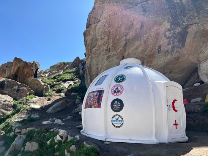A plastic igloo in the shade of a rock by a rocky trail.