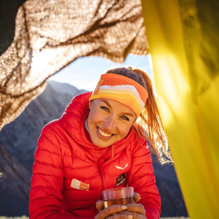 Polackova smiles at a tent's gate with a cup of tea in her hands.