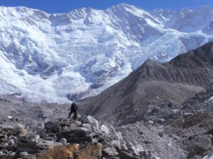 a climber on a pile of stones, in front of a big ice face.