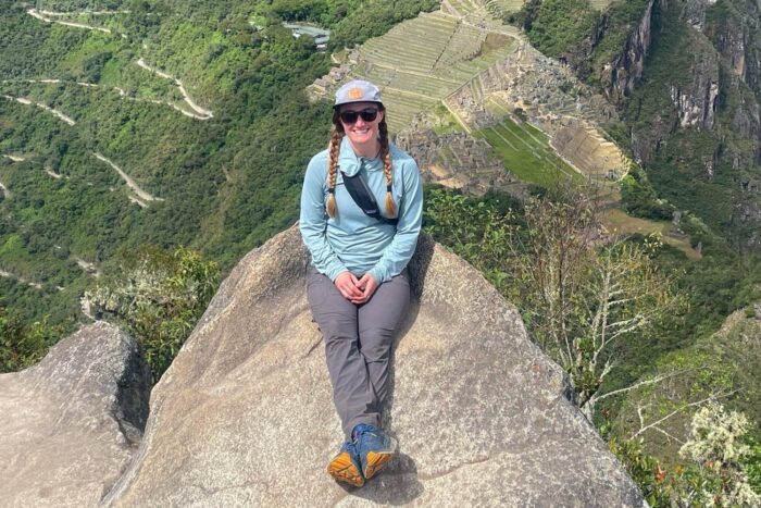 Chelsey is wearing a pair of Arcteryx hiking pants. She's sitting on a rock with Machu Picchu in the background.