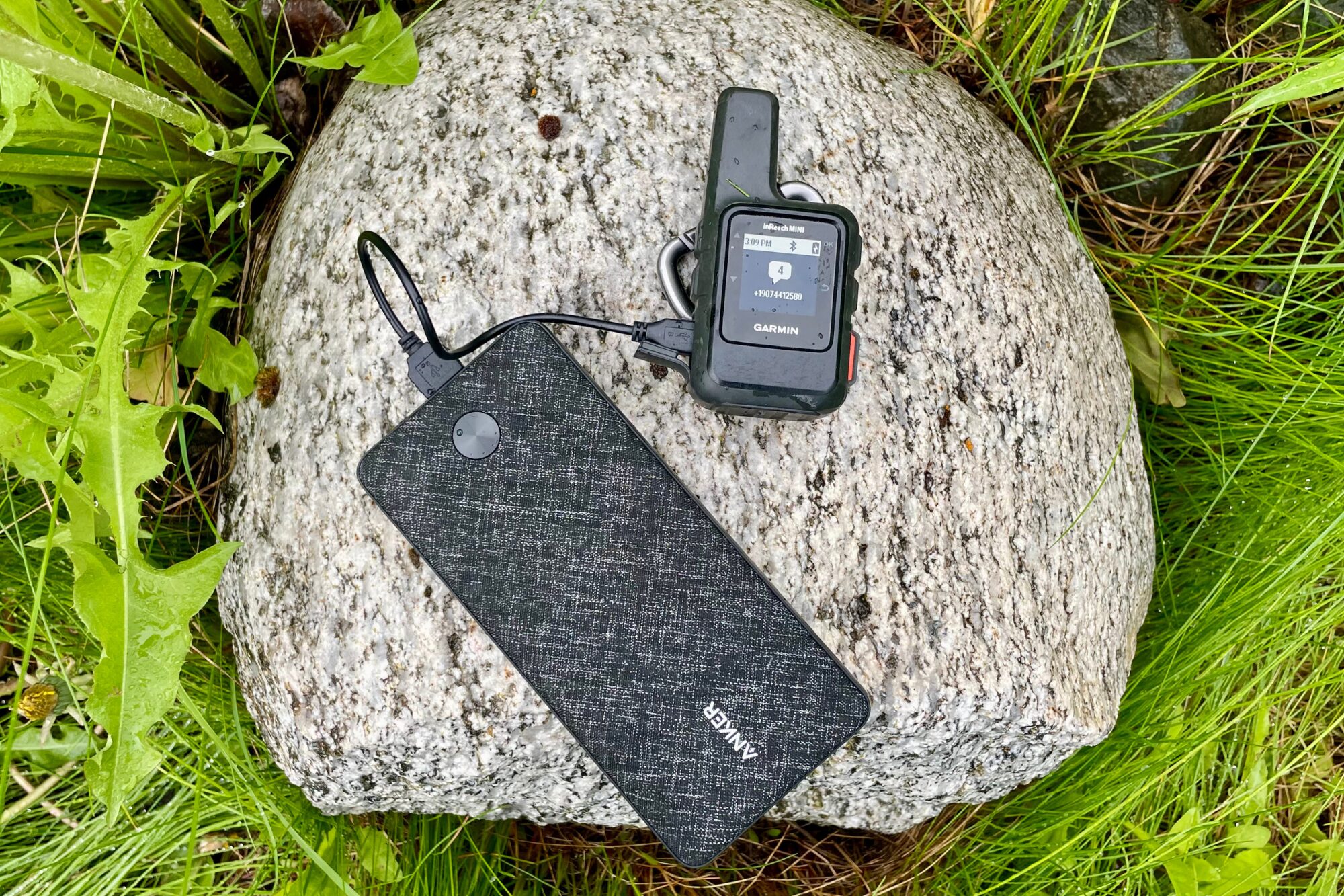 An Anker power bank charges an inReach device, while sitting on a stone.